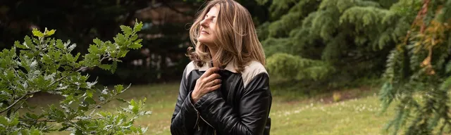 Gabrielle Ladevant, coach et professeure de yoga, assise sur un tronc d'arbre dans la nature, les mains sur le coeur, regard vers le ciel.