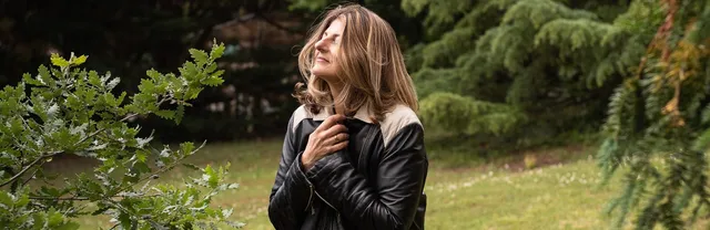 Gabrielle Ladevant, coach et professeure de yoga, assise sur un tronc d'arbre dans la nature, les mains sur le coeur, regard vers le ciel.